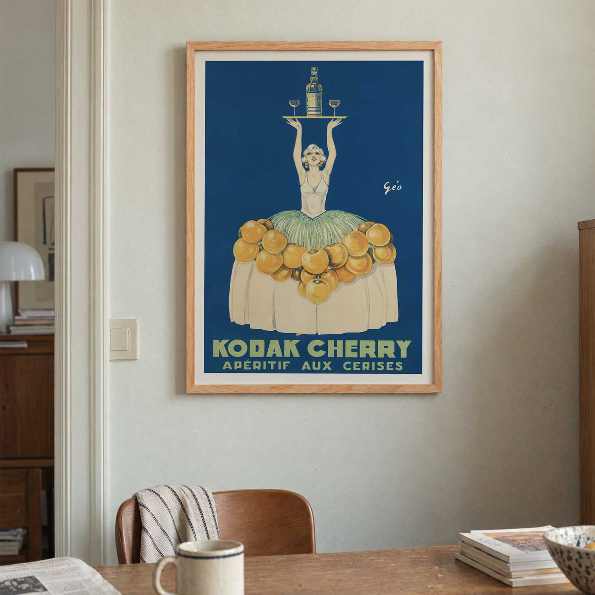Géo Vermeire Kodak Cherry poster with woman in cherry-covered dress holding tray with bottle and two glasses, with wooden magnetic frame on white background