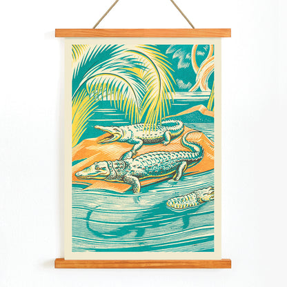 A Jungle Picnic Pl.03 Crocodile by Clifford Webb vibrant jungle artwork and poster showing crocodiles resting by a river under palm trees, with wooden magnetic frame on white background