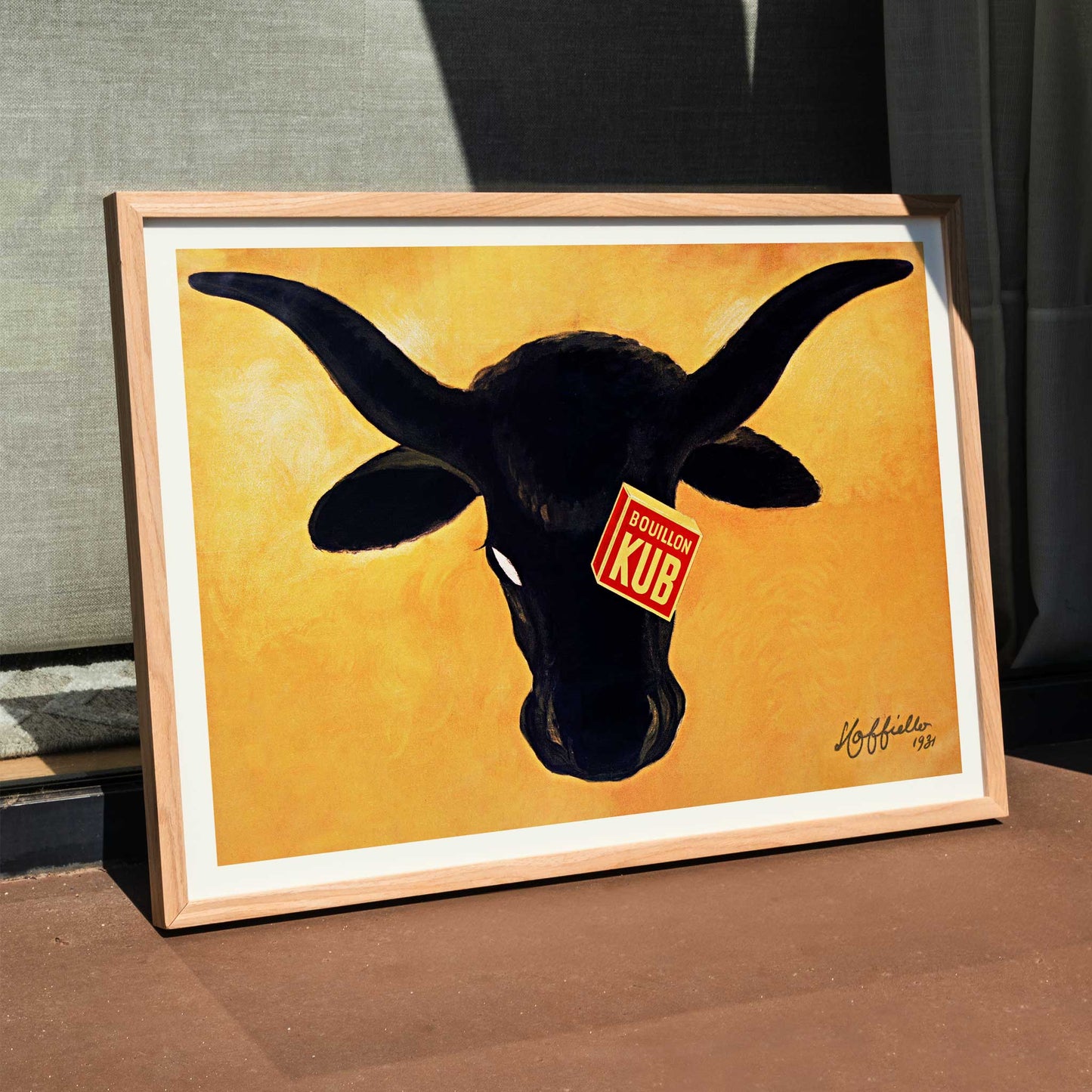 Leonetto Cappiello Bouillon Kub poster featuring a bold black bull on vivid orange background with red label, framed and displayed in modern living room decor