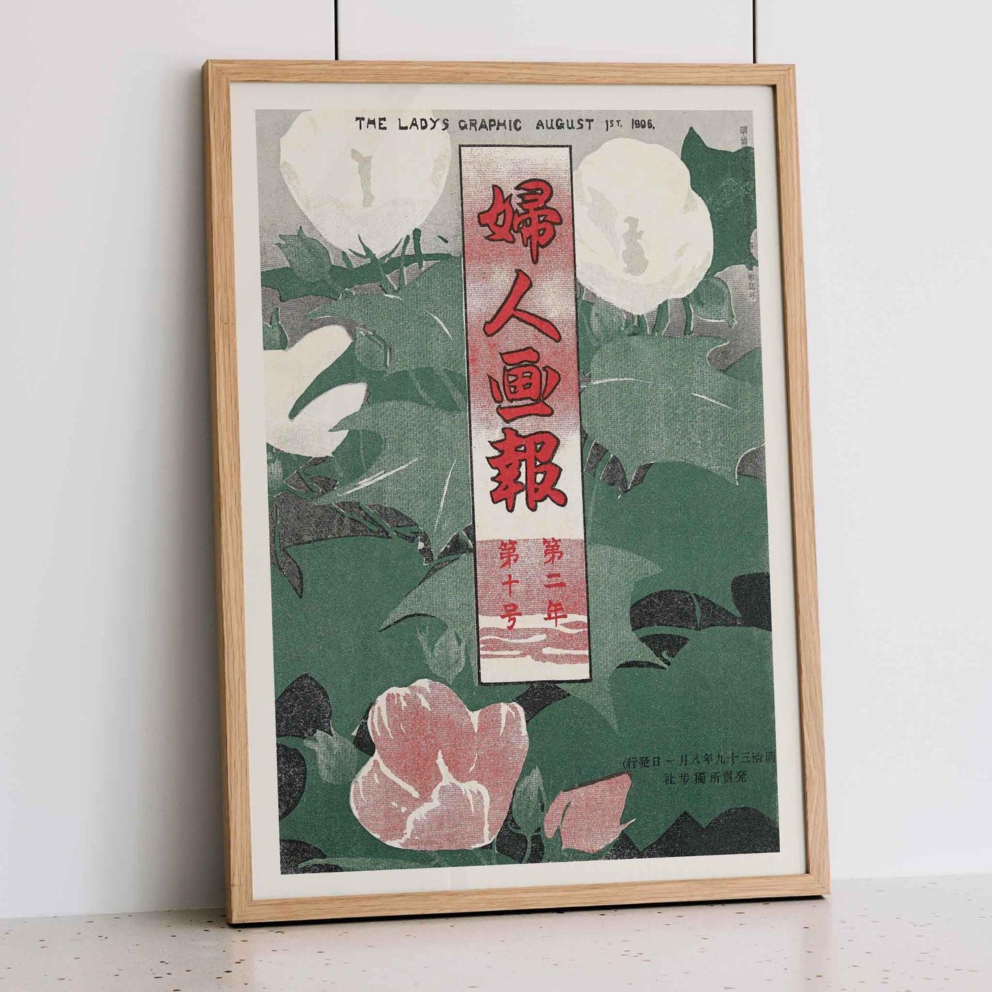 The Lady Graphic by Mitsutani Kunishiro poster with white flowers, green leaves, red lettering, and botanical foliage, framed and displayed in modern living room decor