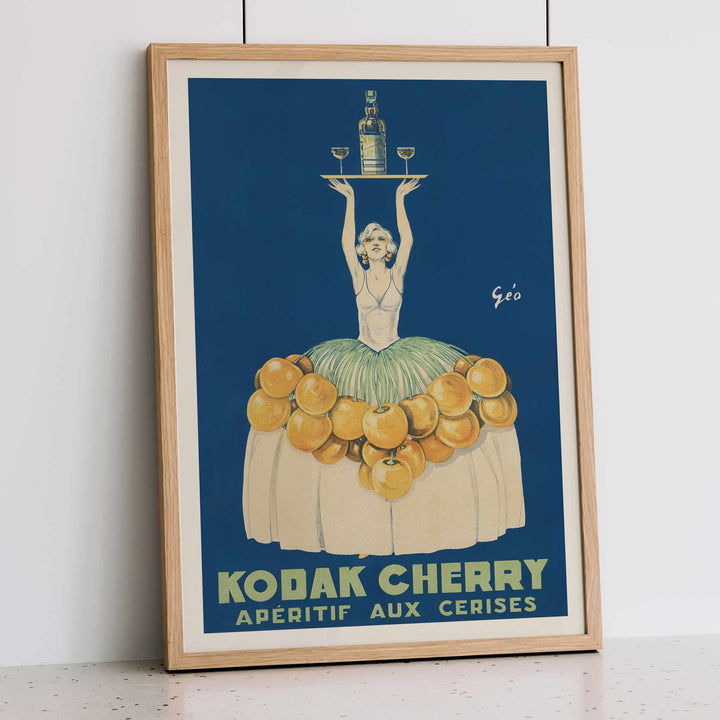 Géo Vermeire Kodak Cherry poster with woman in cherry-covered dress holding tray with bottle and two glasses, framed and displayed in modern living room decor