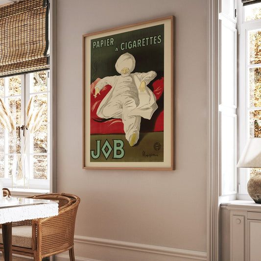 Cigarette Rolling Paper Job poster by Leonetto Cappiello showing a relaxed man in white robes and turban reclining with a cigarette on a red couch, framed and displayed in home decor